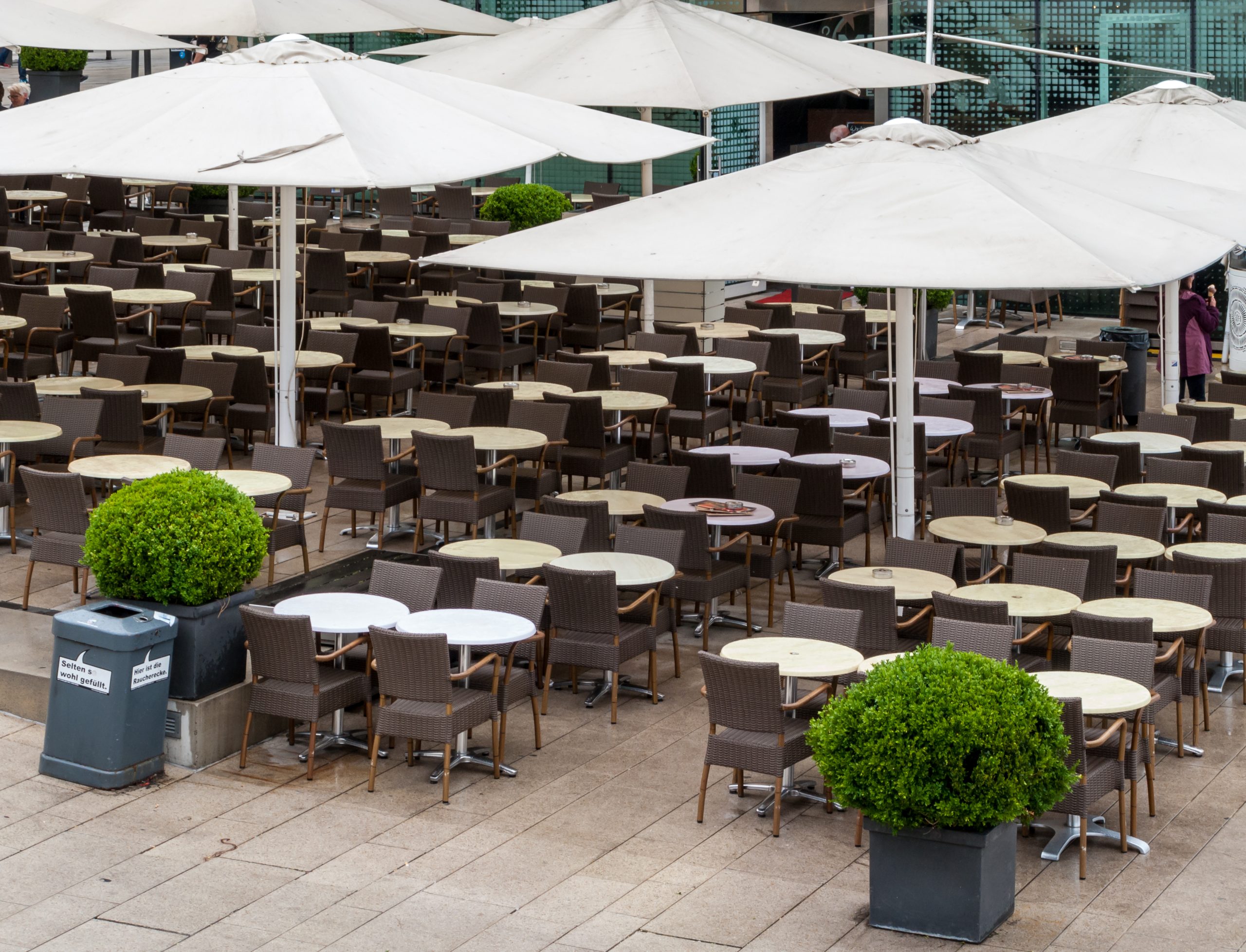 Rows of outdoor restaurant tables and chairs under large white parasols on a city waterfront