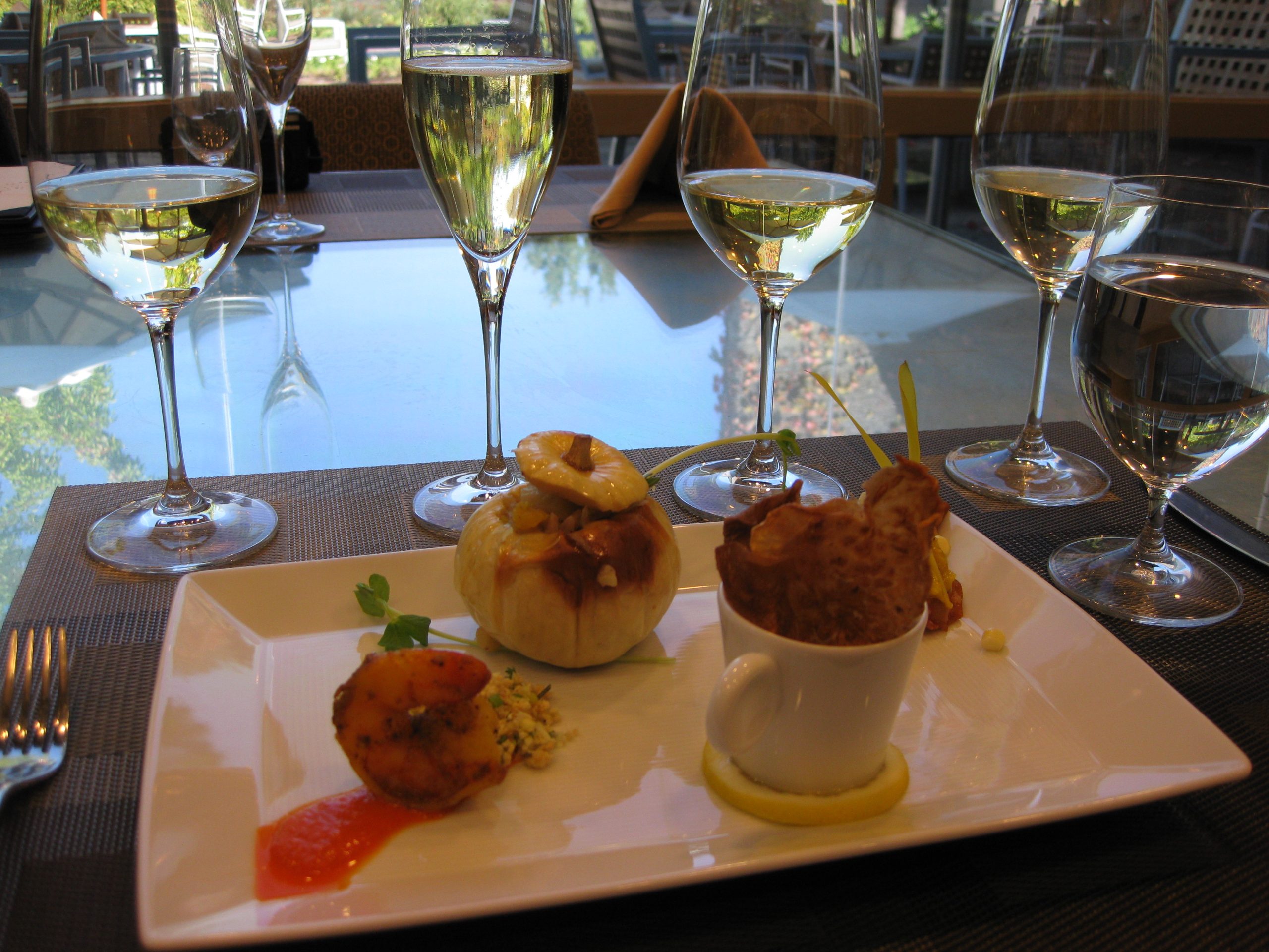 A tasting menu course of three small bites on a square plate, with a glass of wine for each pairing