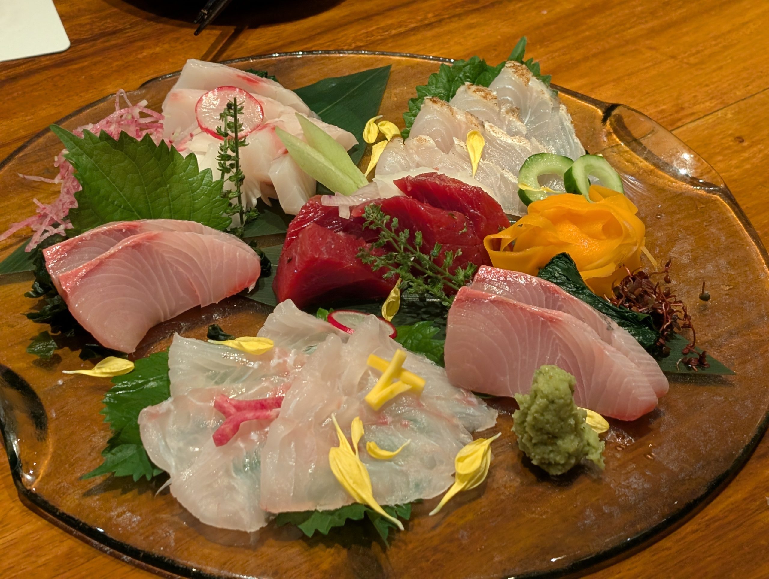A platter of sliced sashimi garnished with shiso leaves and flower petals at a Japanese izakaya