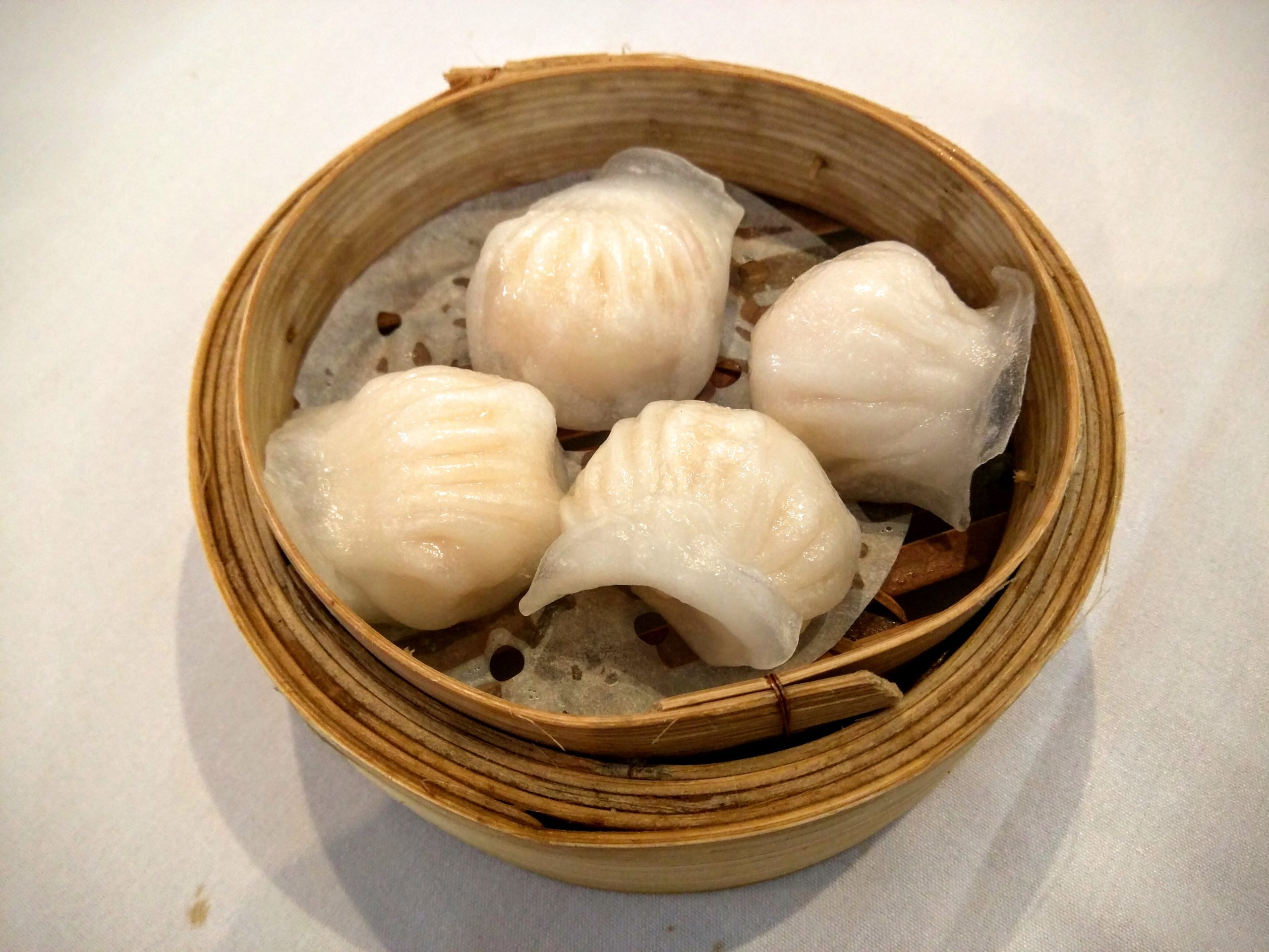 Four steamed prawn dumplings in a small bamboo basket, a light meal for later in the evening