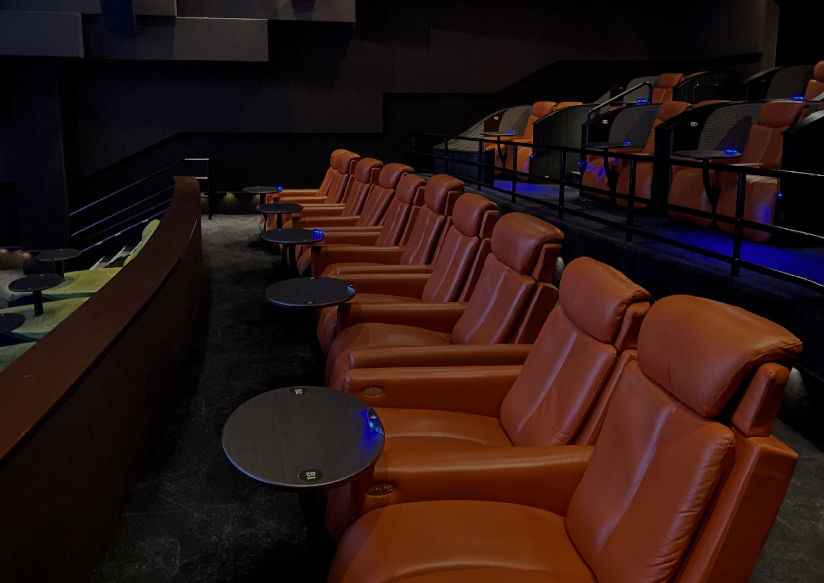 A row of leather reclining cinema seats, each with a small side table for food and drinks