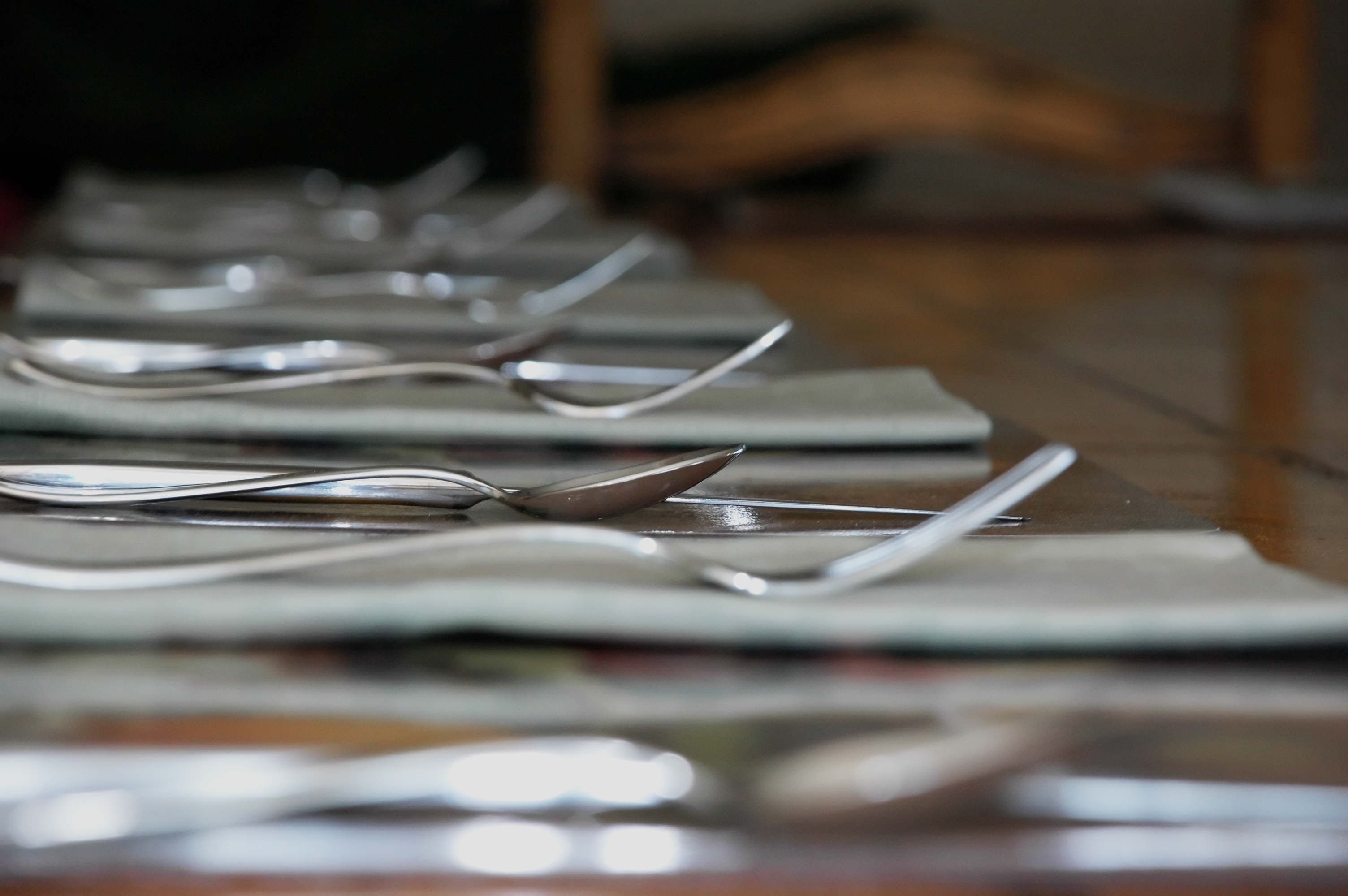 Forks and spoons laid on folded napkins along a wooden dining table
