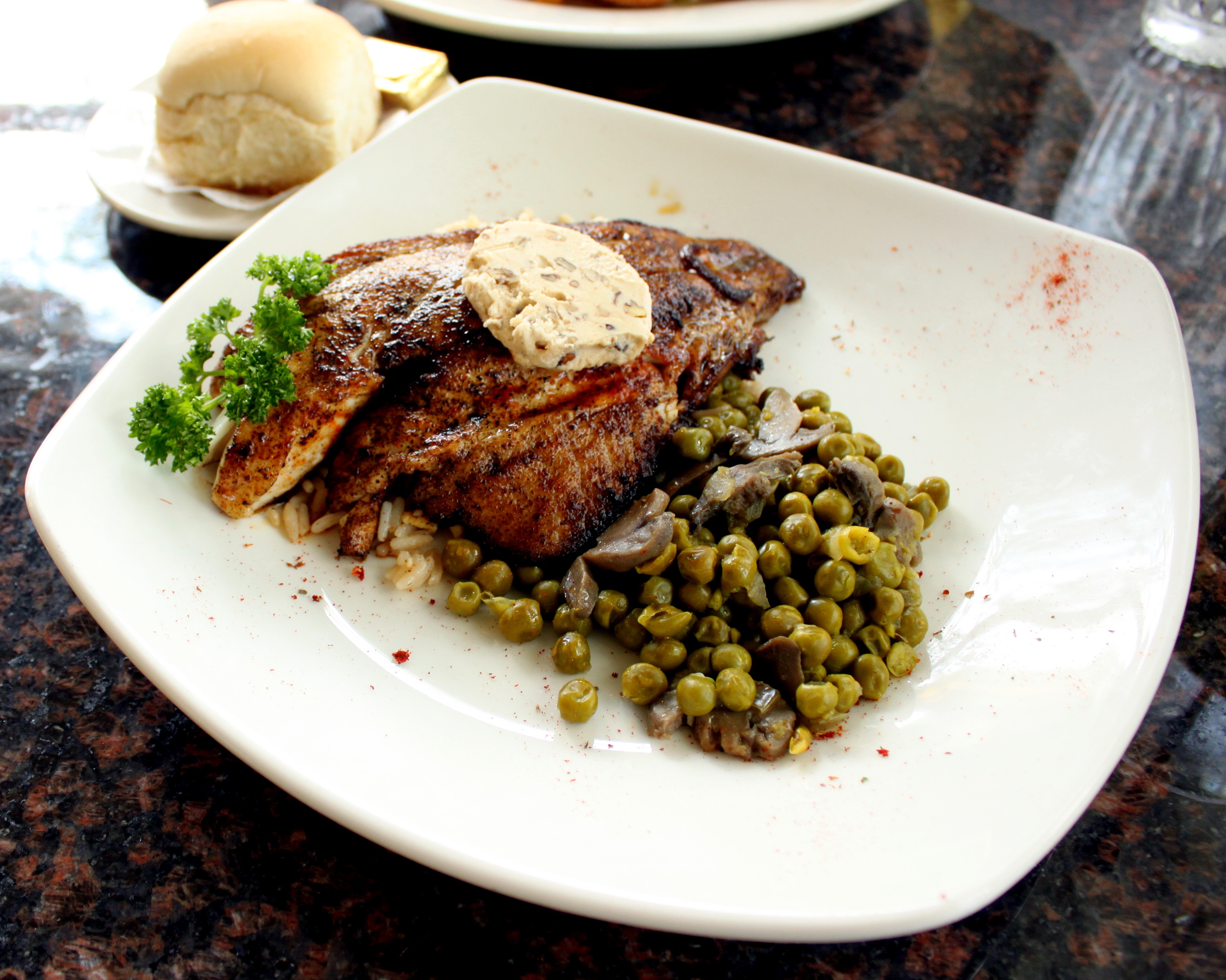 Grilled fish fillet with peas and mushrooms on a square white plate