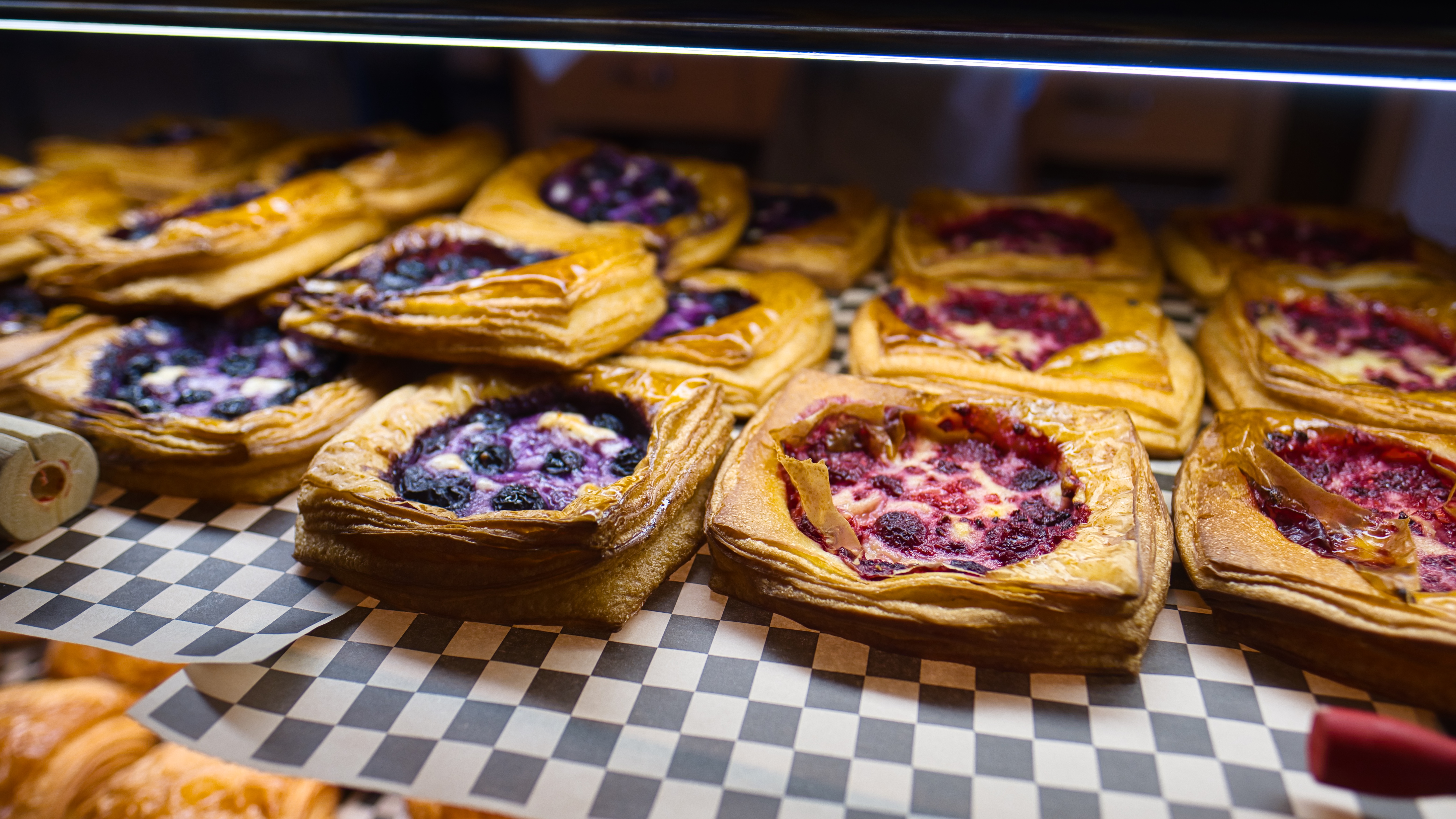 Fruit-filled pastries on chequered paper in a bakery display case