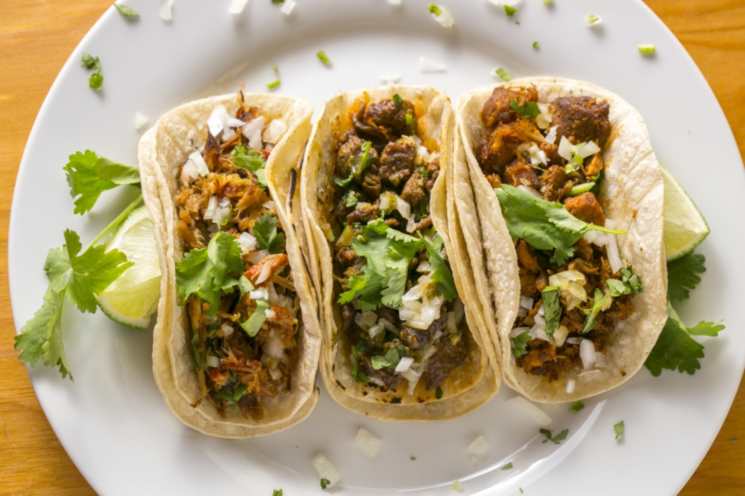 Three soft tacos with chopped coriander and lime wedges on a white plate