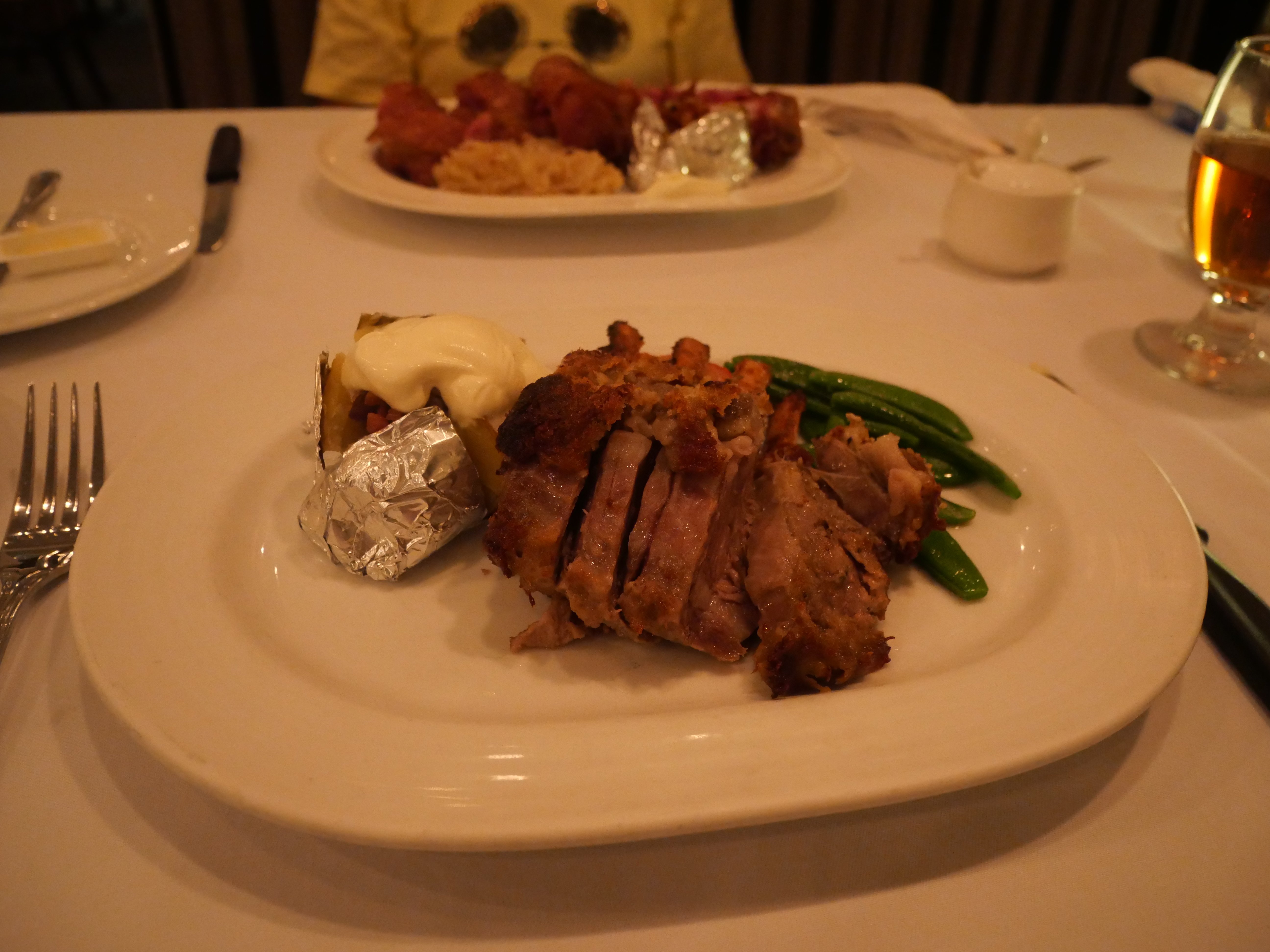 Sliced lamb with a baked potato and green beans on a white plate at a dinner table