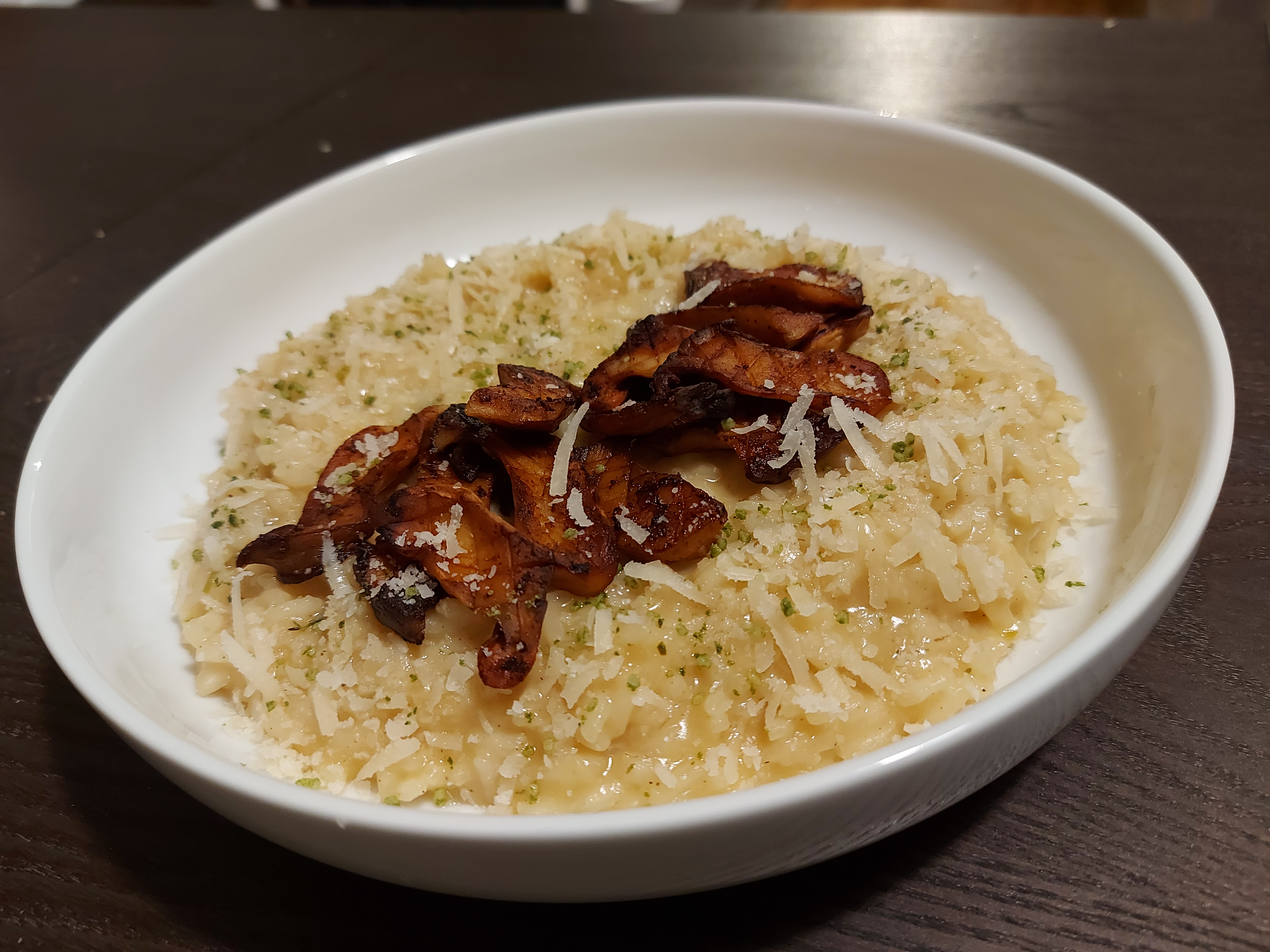 A plate of creamy risotto topped with sautéed mushrooms on a dark wooden table