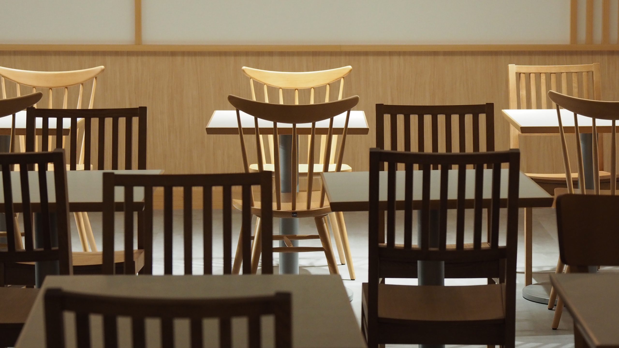 Rows of empty wooden tables and chairs in a quiet, softly lit dining room