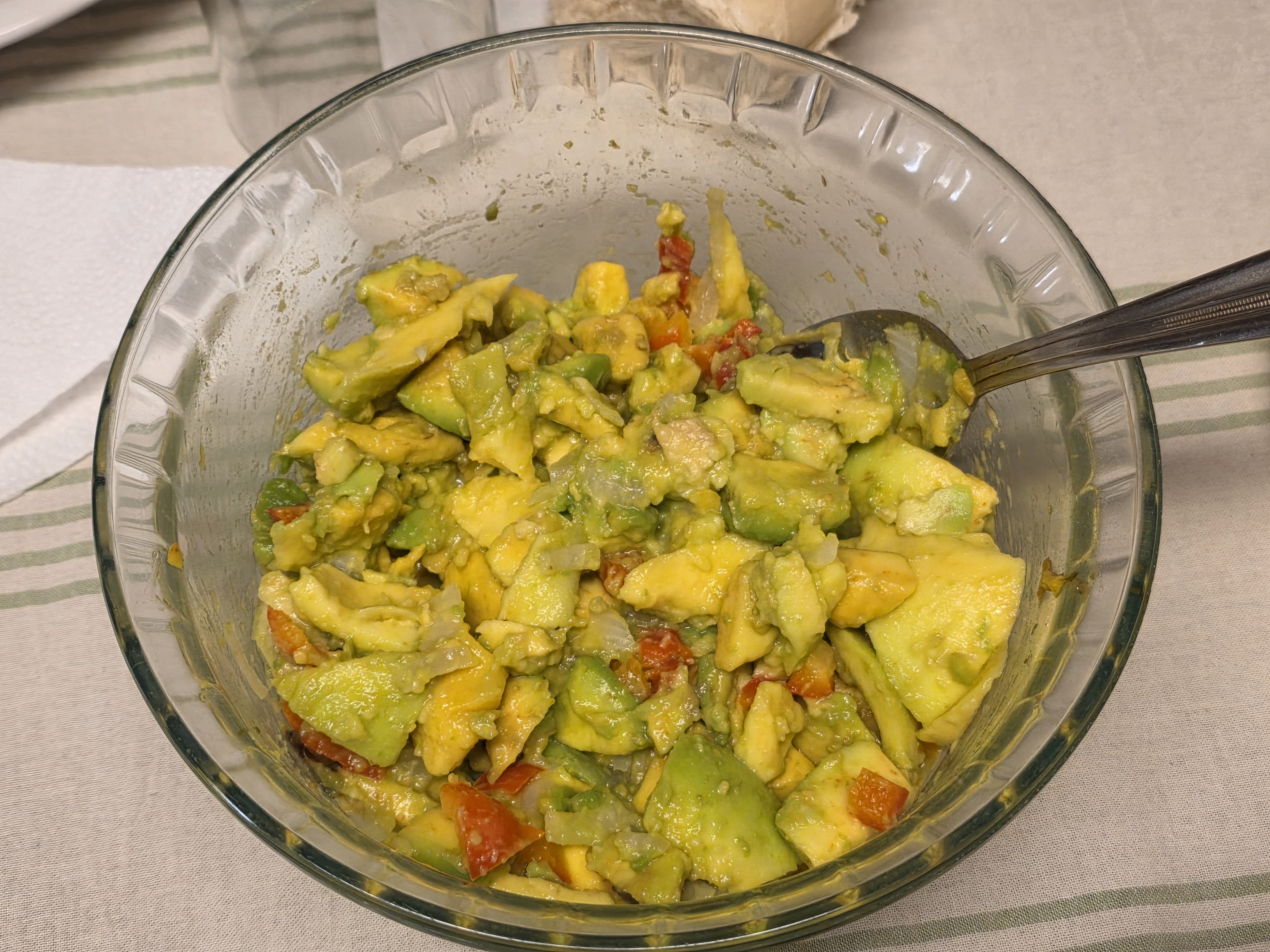 A glass bowl of diced avocado and tomato salad with a serving spoon